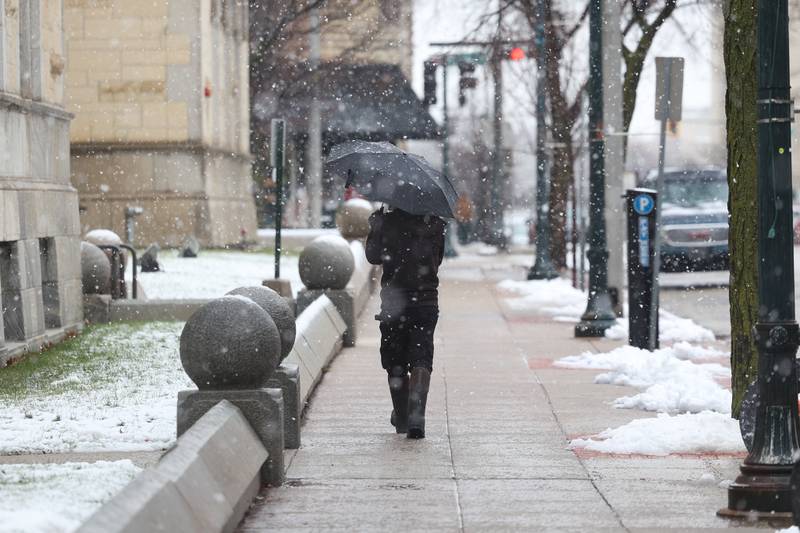 A pedestrian walks down the street with an umbrella in downtown Joliet as afternoon rain turns to evening snow on Tuesday, Jan. 9th, 2024.