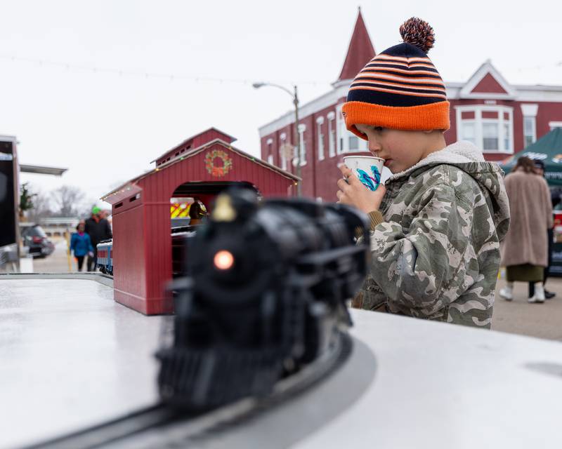 Creed Coss sips hot chocolate as the "Polar Express" toy train drives through tunnel on Saturday, December 6, 2025 on Illinois Avenue in Mendota.