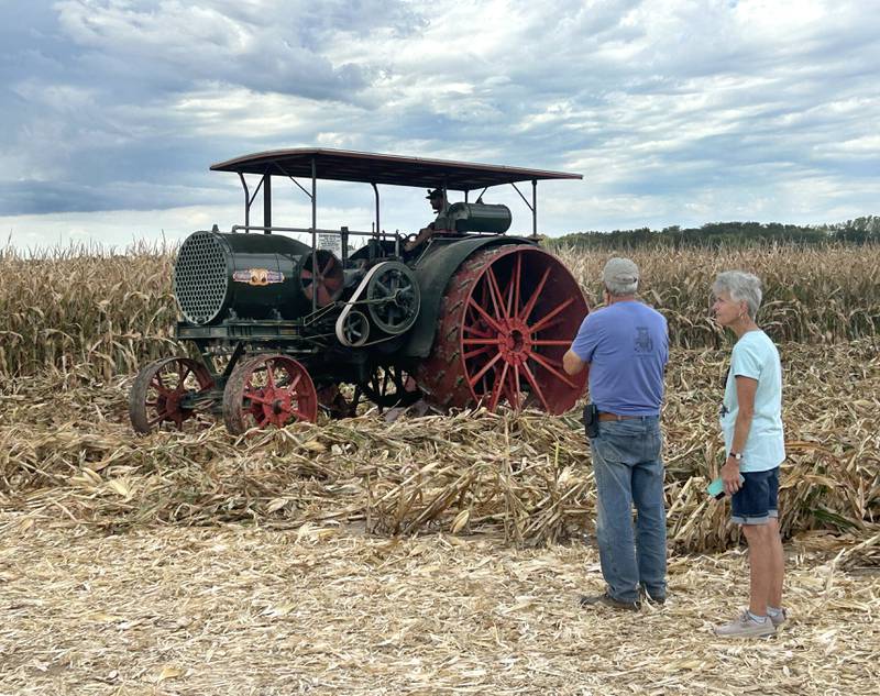 Two people watch as Chuck and Diane Bos's giant Aultman and Taylor kerosene powered antique tractor navigates its way through a corn field at the Bos Bros. Historical Farm Old Fashioned Fall Harvest on Saturday, Sept. 21, 2024. The popular 30-60 was produced from 1910 until the company was sold in 1924. Displays of antique ag equipment and hands-on demonstrations of past agricultural chores were offered at the event.