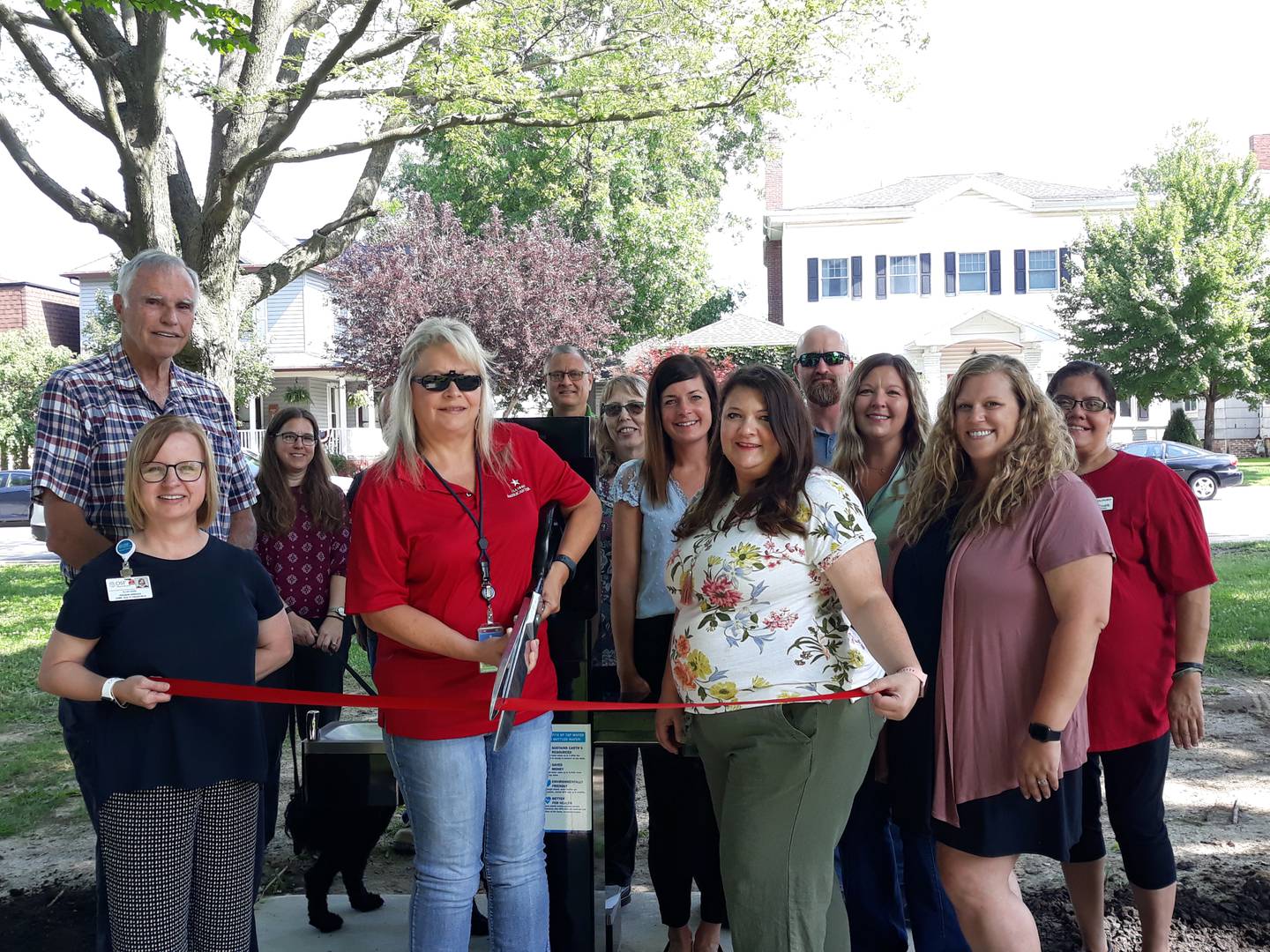 Streator officials cut a ceremonial ribbon Wednesday, July 13, 2022, commemorating the donation of a bi-level drinking fountain in City Park. Participating are (left to right) Ellen Vogel, Live Well Streator; Bob Dieken, Dieken Family Foundation; Elizabeth Palm and her dog Luna; Holly Wheeler (holding scissors), Illinois American Water; Gary Wheeler, Streator Park Board; Judy Booze, Salvation Army and Streator Chamber ambassador; Courtney Levy, Streator Chamber; Mayor Tara Bedei; Jeff Long, Streator Public Works; Dana Stillwell, Streator Chamber ambassador; Megan Wright, Streator Chamber; and Jessica Pastirik.