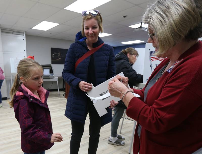 Election judge Adriane Chadwick hands Millie Shanley 6, an "I Voted" sticker while her mom Melissa casts her ballot on Tuesday, Nov. 8, 2022 in Utica.