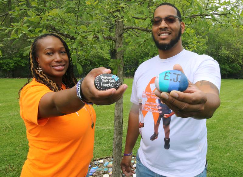 Andrea Elion, mother of Ezra Hill Jr., and Brandon Elion, Ezra’s stepfather, hold painted rocks Monday, May 12, 2025, near the tree and rock garden dedicated to Ezra's memory at Tyler Elementary School in DeKalb. Ezra was shot and killed in 2019 in Harvey. The Ezra Hill Jr. Memorial Rock Painting event will be held June 7 at the school in DeKalb.