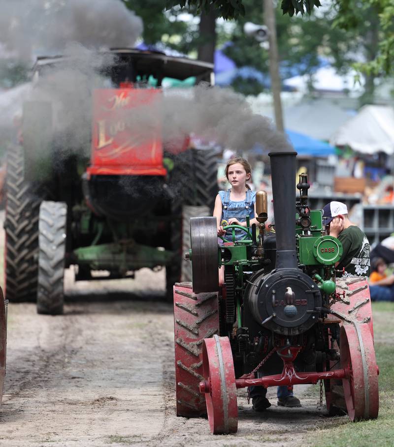 Evalynn Chapman, 8, from Oregon, steers a Case half scale steam engine through the parade with a little help from her grandpa Dave Stevens, from Sycamore, Thursday, Aug. 7, 2025, at the 68th annual Sycamore Steam Show and Threshing Bee at Taylor Marshall Farm on Lukens Road in Sycamore.