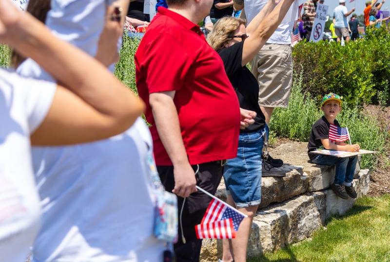 Theo Kannenwischer, 5, sits next to his father with an American flag during a “No Kings Day” Protest against President Donald Trump’s policies along South Randall Road in Geneva on Saturday, June 14, 2025. Kannenwischer’s father is an immigrant from Germany and Theo is a dual citizen of both the United States and Germany.