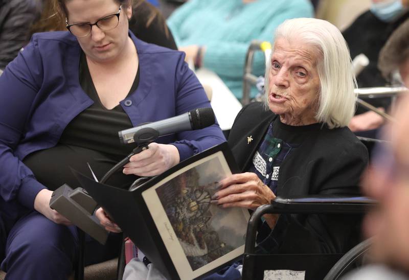 Mary Roman, a resident of the DeKalb County Rehabilitation and Nursing Center for seven years, speaks during public comment as Ashley Rockstead, assistant director of nursing at the center, holds the mic at the DeKalb County Board meeting Wednesday, April 20, 2022, in the legislative center in Sycamore. One of the items on the agenda was to vote on whether to sell the DeKalb County Rehabilitation and Nursing Center.