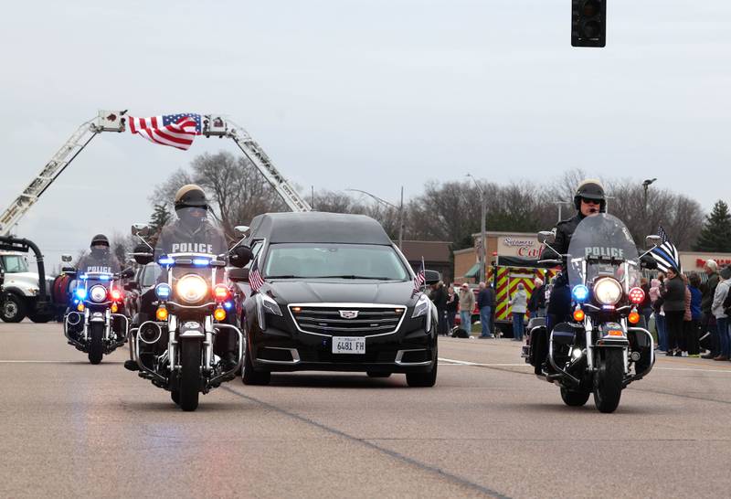 The hearse carrying the body of DeKalb County Sheriff’s Deputy Christina Musil goes under ladder trucks from the DeKalb and Shabbona Fire Departments Monday, April 1, 2024, on DeKalb Avenue in Sycamore during a processional to honor the fallen officer. Musil, 35, was killed Thursday while on duty after a truck rear-ended her police vehicle in Waterman.