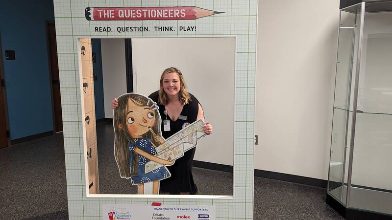 Mallory Hewlett, communications manager at the Joliet Public Library, poses with her favorite character in “The Questioneers: Read. Question. Think. PLAY!” exhibit on Wednesday, June 21, 2023. This exhibit is based on the Questioneers book series authored by Andrea Beaty and illustrated by David Roberts. This traveling exhibit featuring the Questioneers characters opened June 16 at the Ottawa Street branch of the Joliet Public Library and is available during library hours through July 29.