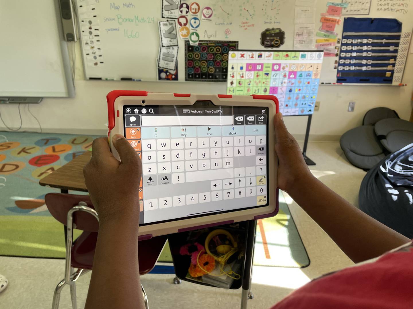 A student is seen holding an Augmented Alternative Communication (AAC) device in hand.