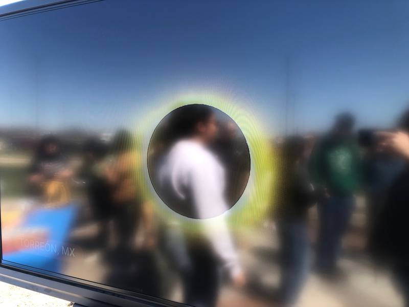 A NASA feed from Mexico showing the total eclipse is shown on a screen during a viewing event at McHenry County College in Crystal Lake on April 8, 2024, with participants shown. in the reflection.