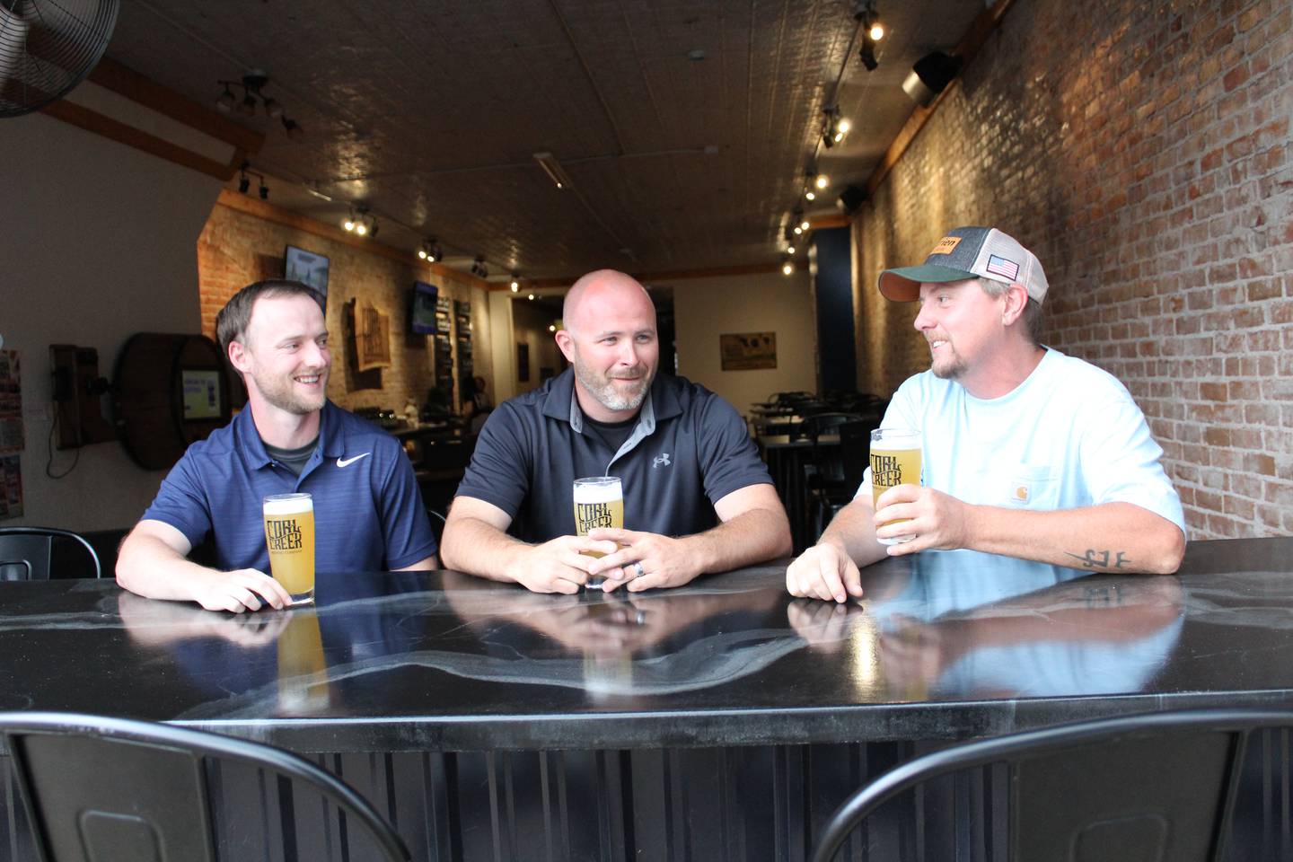 Trevin Kennedy (from left), Michael Grieve, and Justin Stange, owners of Coal Creek Brewery in Princeton, sit at the open-air bar area at the brewery.
