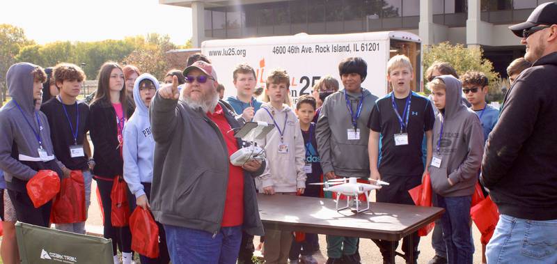 Eighth-grade students from Byron gather around an agricultural drone demonstration conducted by Sauk Valley Community College's Michael Selover, pointing, and Kevin Larsen, far right, on Friday, Oct. 14, 2022, during the Pathway Playground career fair. The pair demonstrated how drone sensors can identify pest-infested and diseased crops in a field, then downloads that information to a tractor's computer so that it applies chemical sprays only on affected areas — a more efficient and economical method of intervention.