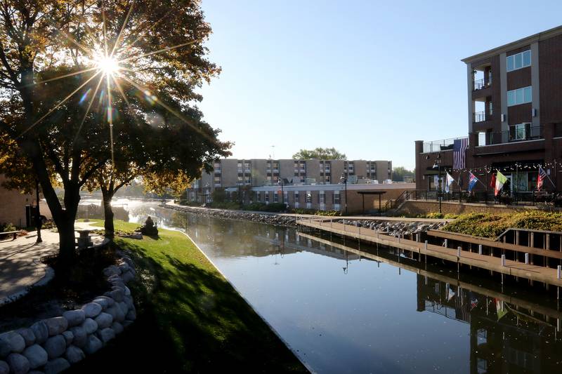 The morning sun pokes through the changing autumn leaves as a man mows the grass next to DC Cobbs and the McHenry Downtown Indoor Theater, along the Fox River at the McHenry Riverwalk on Thursday, Oct. 8, 2020 in McHenry.