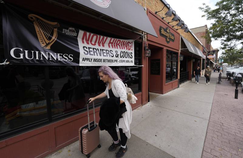 FILE - A traveller wheels her baggage past a now hiring sign outside a bar and restaurant Saturday, Oct. 9, 2021, in Sioux Falls, S.D.  America’s employers slowed the pace of their hiring in November, adding 210,000 jobs, the lowest monthly gain in nearly a year.   Friday, Dec. 3 report from the Labor Department also showed that the nation's unemployment rate tumbled from 4.6% to 4.2% evidence that many more people reported that they had a job.