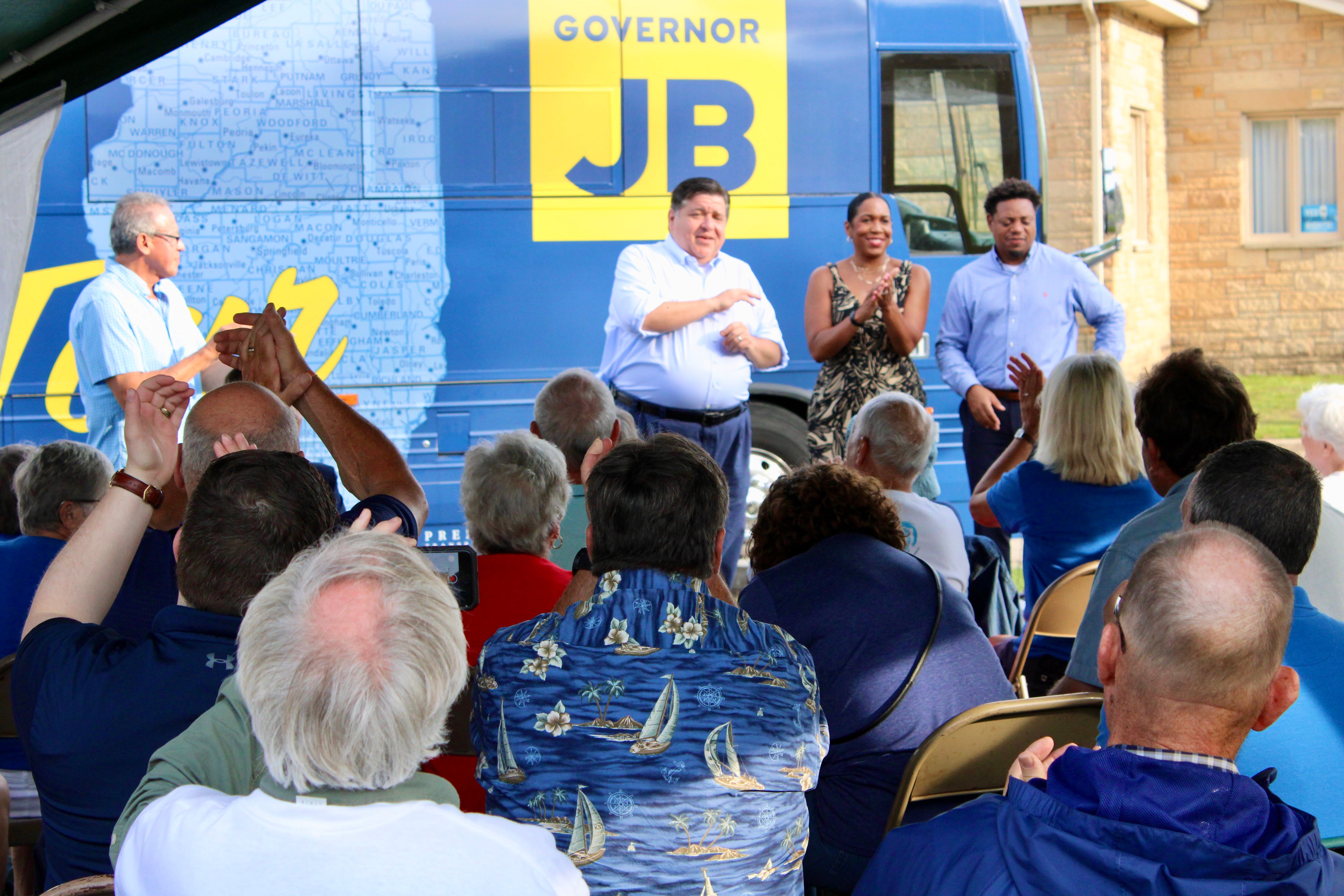 A crowd of about 70 people applauds as Gov. JB Pritzker makes a campaign speech on Sunday in from of his tour bus parked in front of the Whiteside County Democratic Headquarters in Rock Falls. From left: Whiteside County Democratic Chairman Fidencio Campos, Pritzker, Lt. Gov. Juliana Stratton and her husband, Bryan Echols.