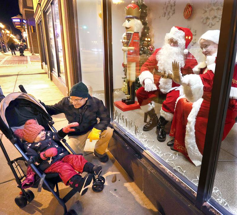 Dave Smith and his daughter Sterling, 3, from Sycamore, wave to Santa and Mrs. Claus in the window of Sycamore Center Friday, Nov. 18, 2022, during the Sycamore Chamber of Commerce's annual Moonlight Magic event in downtown Sycamore.