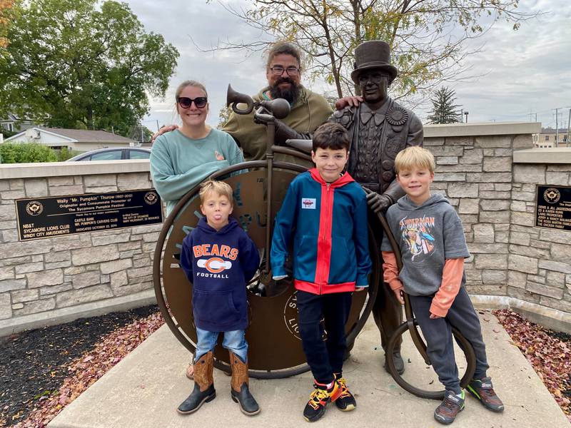 Harrison Rowland, 8, of Sycamore (front middle), poses with his family (from left: Mom Sarah Rowland, brother Lincoln Rowland, Dad David Rowland and brother Emmitt Rowland) in front of the Wally Thurow statue in Sycamore Friday, Oct. 6, 2023. Harrison is the theme contest winner for "Pumpkins of History" for the 2023 Sycamore Pumpkin Festival.