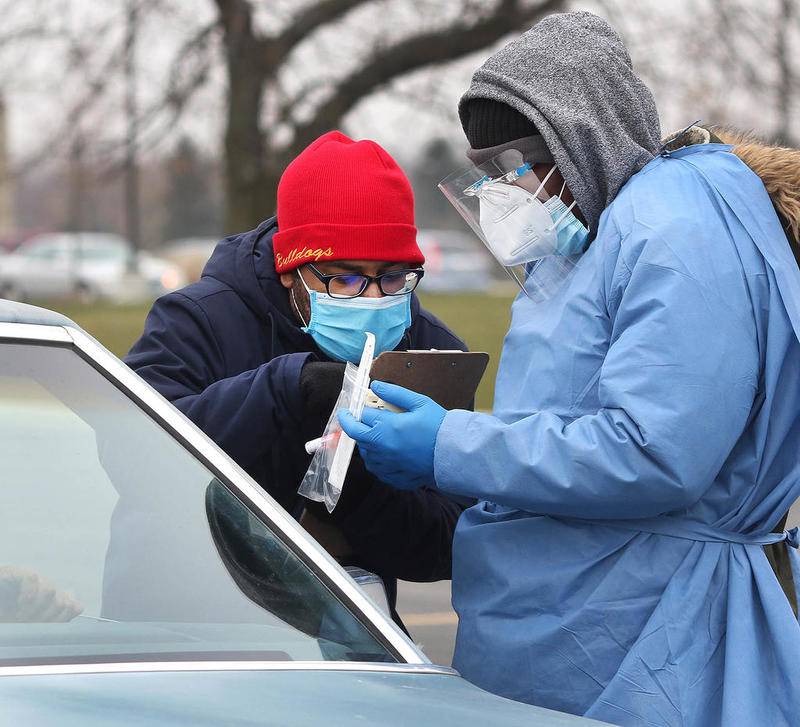 Enrique Jones, (left) an HR Support site manager, and Adebayo Adeniyan, a phlebotomist from HR Support, take a sample from a patron on a cold Tuesday afternoon at the COVID-19 testing location in the parking lot at the Kishwaukee Family YMCA in Sycamore.