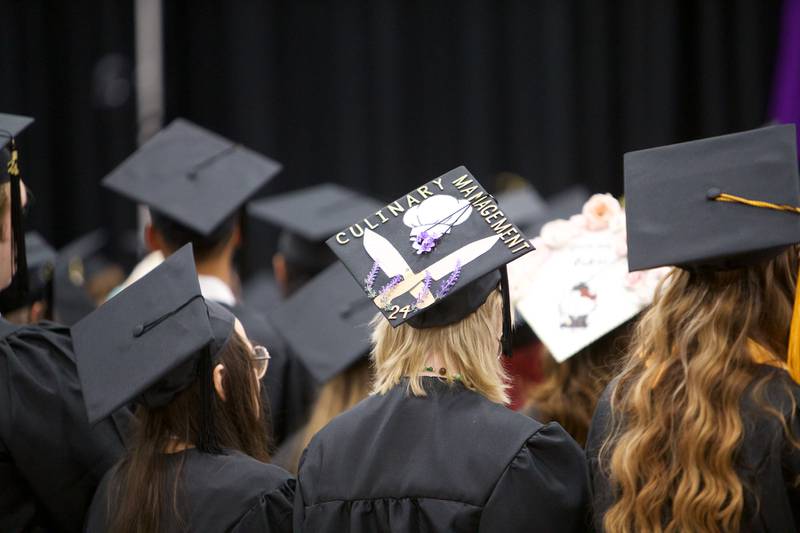 A culinary management graduate's cap includes images of knives and a chef's hat during McHenry County College commencement on Saturday, May 11, 2024, in Crystal Lake.
