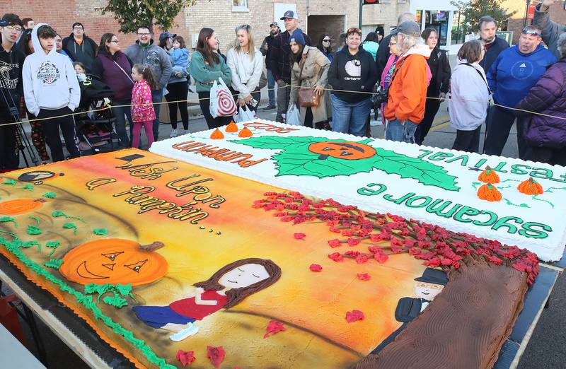 People gather around the large cakes donated by Hy-Vee during the cake cutting ceremony Wednesday, Oct.26, 2022 on North Maple Street near the DeKalb County Courthouse during the first day of the Sycamore Pumpkin Festival.