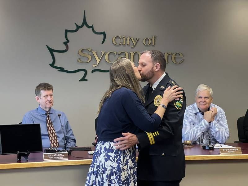 Sycamore City Manager Michael Hall and Mayor Steve Braser react as Ryan Hooper and his wife, Tracy Hooper, kiss after Hooper was promoted to the Sycamore Police Department's second-highest position on July 21, 2025.