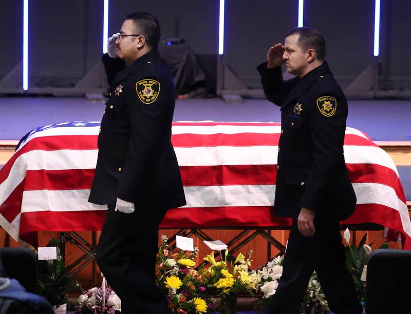 Law enforcement officers salute as they pass by the casket of former DeKalb County Sheriff Roger Scott during a law enforcement walk-through at the visitation for Scott Thursday, March 6, 2025, at Bethany Road Bible Church in DeKalb. Scott, who was the county sheriff for more than 30 years, died on February 23 at the age of 78.