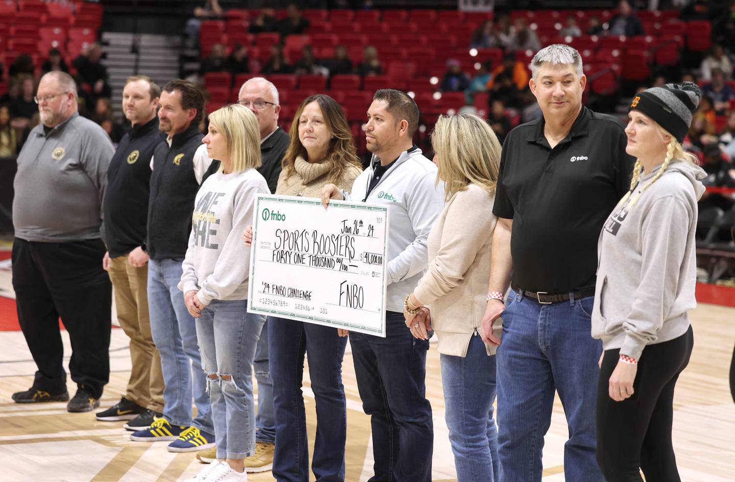 DeKalb and Sycamore boosters and staff along with members of FNBO pass a check Friday, Jan. 26, 2024, for $41 thousand dollars that was collected for this years event during the FNBO Challenge in the Convocation Center at Northern Illinois University.