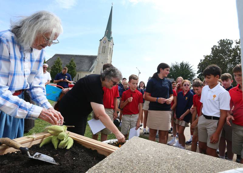 (From left) Nancy Maze and Cindy Pasieka hands wildflower seeds to students at Academy of Saint Carlo Acutis on Friday Aug. 29, 2025 in Peru. Maze and Pasieka taught students how to plant wildflower seeds and native prairie flowers. The Peru Historical Society assisted with the seed planting. Debo Ace Hardware also donated supplies.