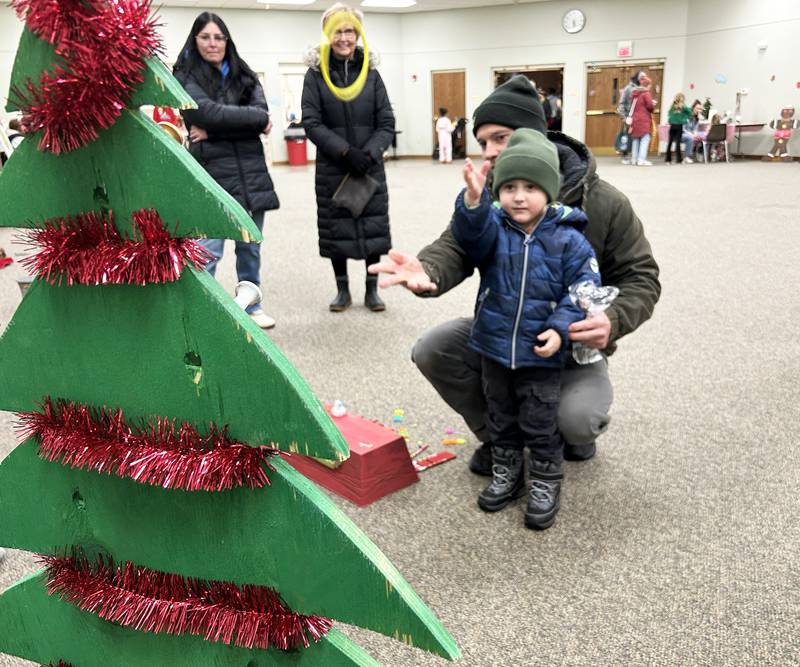 Tate Klotz, 3, of Oregon, tosses a ring at a Christmas tree with the help of his dad, Kyle, at Oregon Candlelight Walk's Kid's Winter Carnival held at the United Methodist Church on Saturday, Dec. 6, 2025.