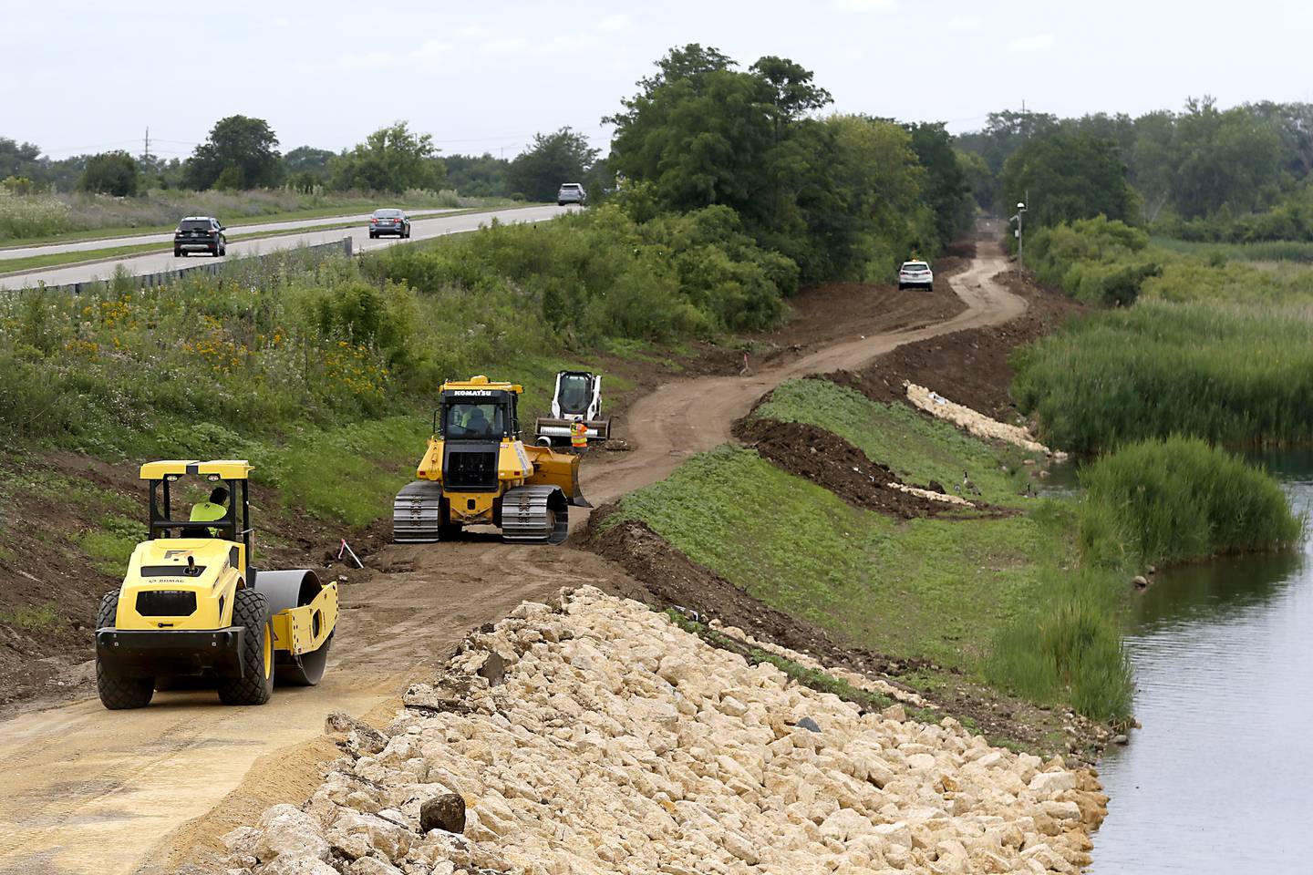 Work continues on a walking path around the lake at Three Oaks Recreation Area on Thursday, July 24, 2025, near the intersection of Pingree and James R. Rakow roads. When all the construction is complete there will be a 3.1 mile loop around the lake.