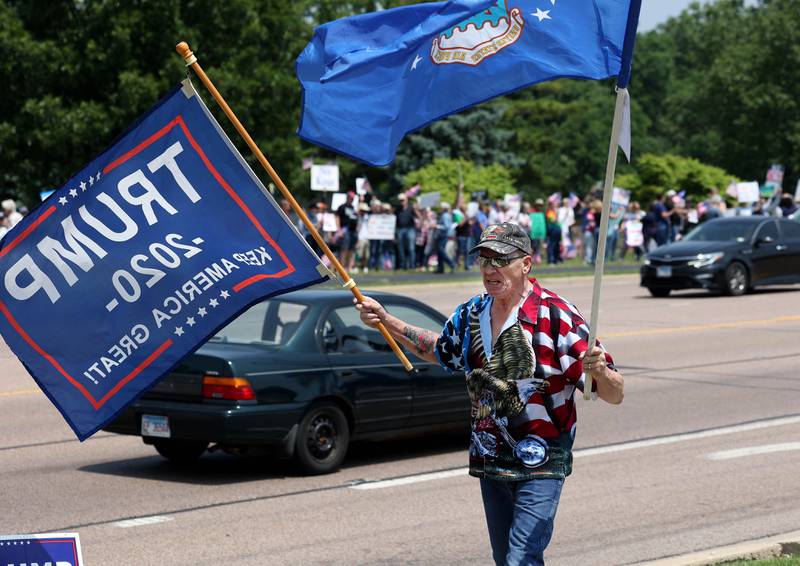 Steve Bellows, from DeKalb, a supporter of President Donald Trump carries flags Saturday, June 14, 2025, during a No Kings rally along Sycamore Road at Hopkins Park in DeKalb. The group was protesting the policies of President Donald Trump and his administration.