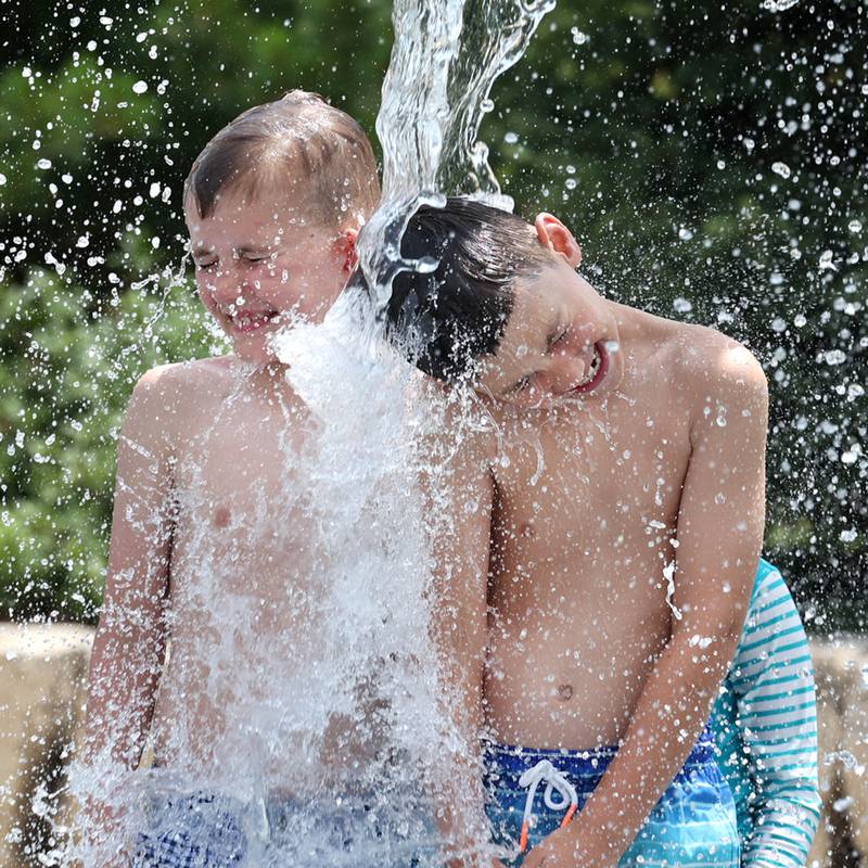 Rhett Hintzsche (left) and Bo Burdick, both 8, from Sycamore, get a bucket of water on their heads Thursday, June 20, 2024, at Splash Fountain Splashpad at the Sycamore Park District’s Legacy Campus on Airport Road. High temperatures have been over 90 degrees every day this week making splash pads and pools very popular destinations.
