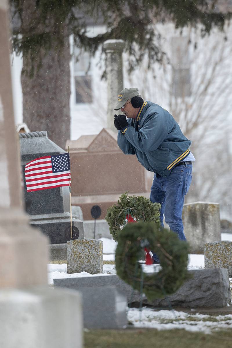 Dennis Moss warms his hands Saturday, Dec. 13, 2025, after placing a wreath at Palmyra Cemetery.