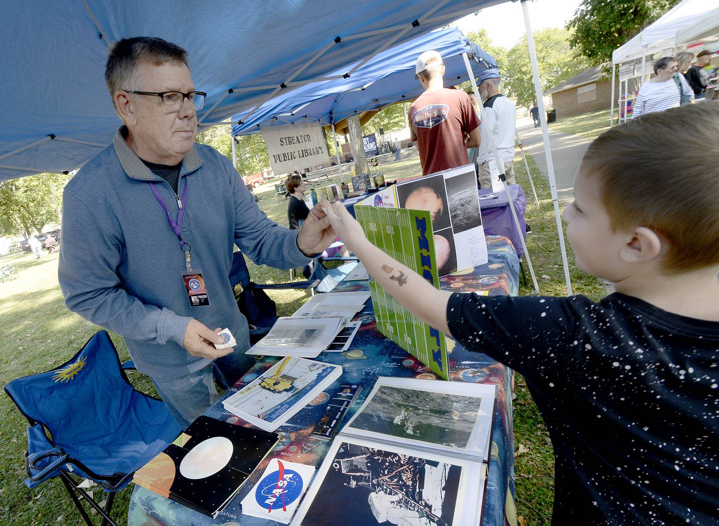 Solar System Ambassador for NASA Scott Pelican hands a NASA sticker to Maddux Johnson on Saturday, Sept. 24, 2022, during Pluto Fest at City Park in Streator.