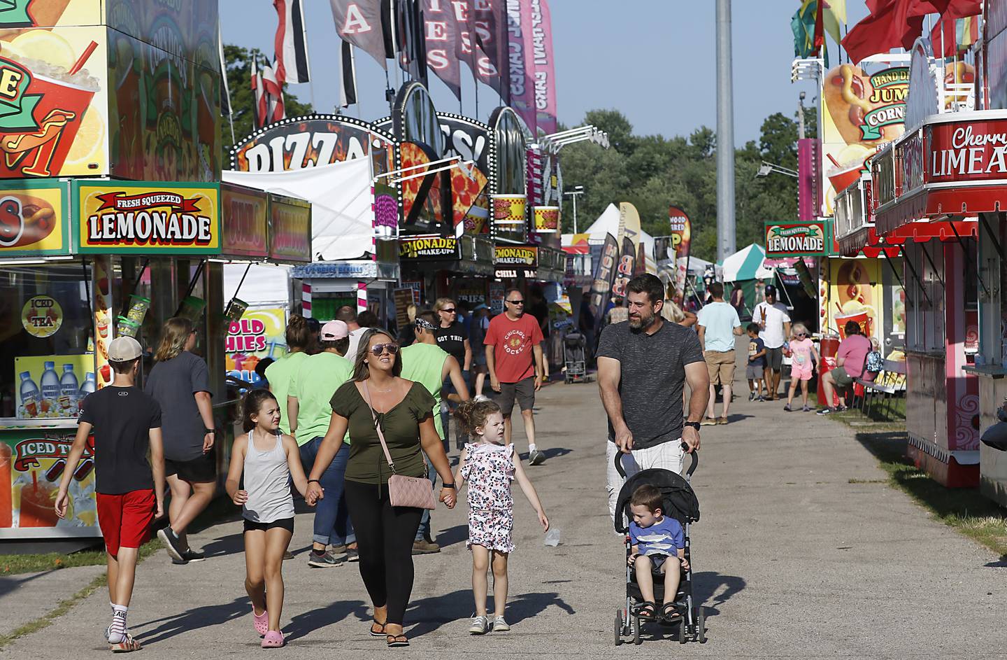 A family walks down the midway during the first day of the McHenry County Fair Tuesday, August 2, 2022, at the fairgrounds in Woodstock. The fair funs through Sunday, Aug. 7.  Entry to the fair is $10 for anyone over age 14, and $5 for chidden ages 6 to 13. Ages 5 and under are free.