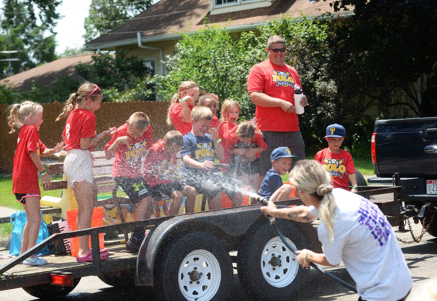 Montana Muntean uses Billie Quaco's garden hose to soak her daughter's youth baseball team as the team drives past Quaco's home during the Town & Country Days Parade on Sunday, June 29, 2025.