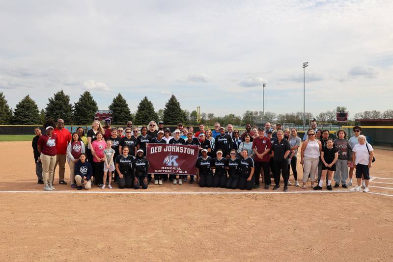 Kankakee High School players, staff, family and friends of the late Deb "Coach. J" Johnston pose for a photo with the new banner designating the softball field as the Deb Johnston Memorial Softball Field on Wednesday, May 7, 2025.