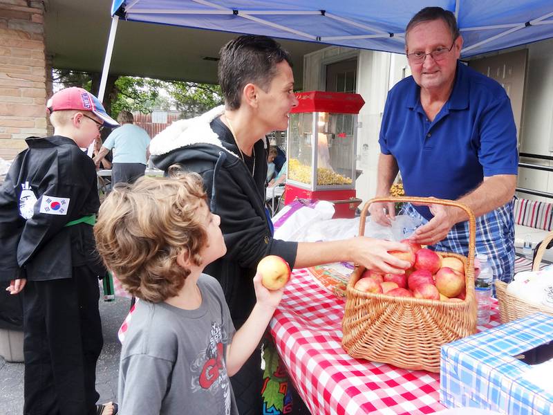 Verle Rueff (right) gives apples to Julie Wright and her son Juliano Wright, both of Shabbona, at the open house wellness event of the United Neighborhood Center in Shabbona on Saturday, Sept. 20.