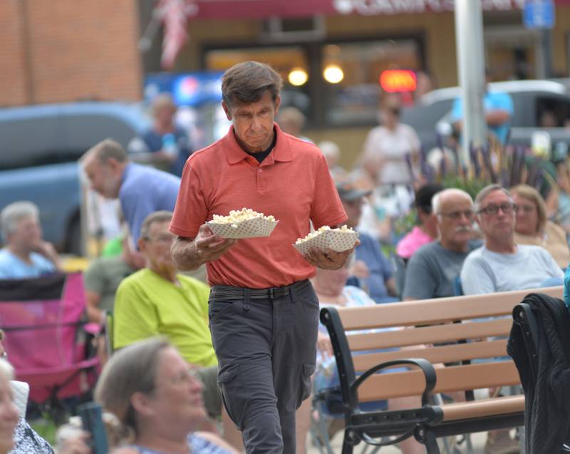 Fresh popcorn is one of the food items offered during the free Jamboree concerts in Mt. Morris each Friday night. Here, a visitor carries back two bowls of popcorn provided by the Mt. Morris Senior and Community Center. Captain Rat and the Blind Rivets played rock and roll hits from the 1950s and 1960s at the  Friday, Aug. 15, 2025 concert.