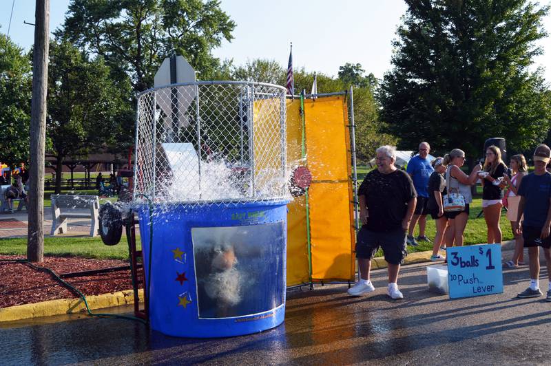 Chuck Collis, of Rockford, (center) watches as Keynan Janicke falls into the dunk tank after he pushed the lever on Friday, Aug. 2, 2024, during Forreston Sauerkraut Days. Collis paid to push the lever twice.