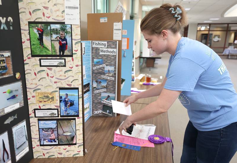 Lydia Nickels, office support assistant with the U of I Extension, places ribbons at winning entries in the 4-H General Project Show Thursday, July 14, 2022, at the DeKalb County Farm Bureau in Sycamore.