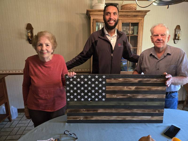 Retired Army Combat Engineer Thomas Ewertowski (right) is shown with his wife, Barbara, and Michael Adams, a U.S. Marine veteran and Bremer Team - Keller Williams Success Realty agent. Ewertowski is one of 30 McHenry County veterans selected as a 30 Days for 30 Vets program recipient. Above Par Construction supplied flag plaques for all honorees.