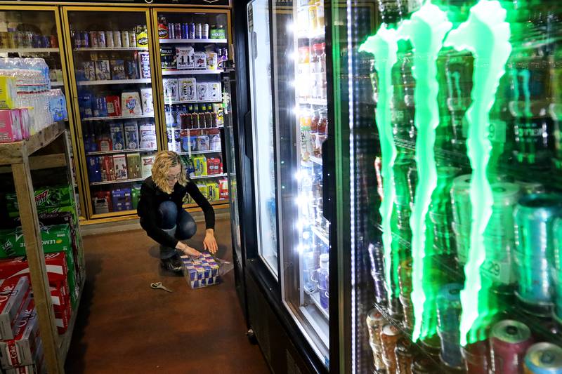 Store clerk Pam Donzelli stocks the refrigerated coolers with beverages at Creekside Country Store on Wednesday, Dec. 16, 2020, in Wonder Lake.