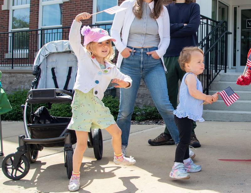 Ellie Jo Didier, 4, and Ana Mey Didier wave their flags and dance while St. Charles North’s band performed during the St. Charles Memorial Day Parade in downtown St. Charles on Monday, May 26, 2025.