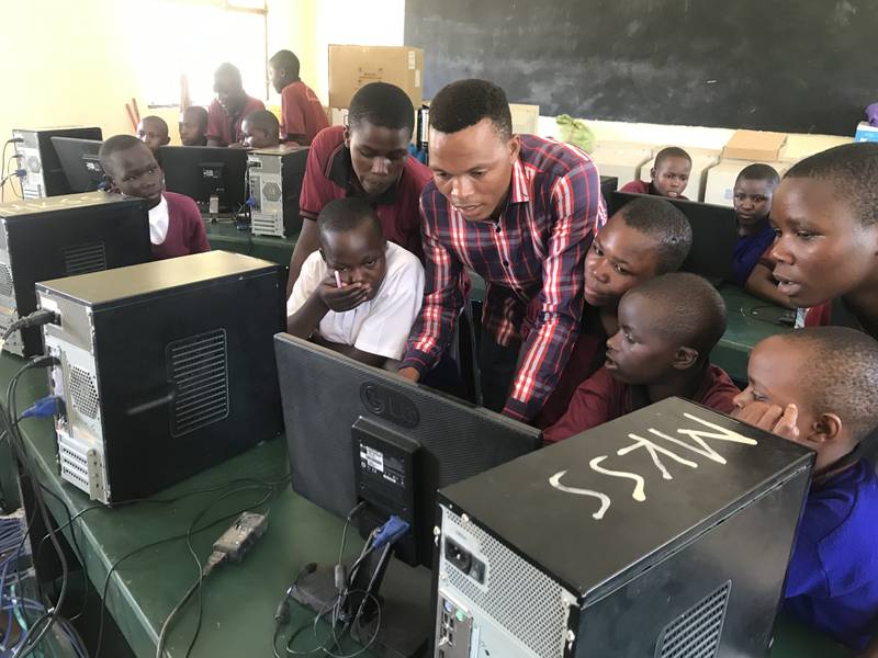 John Kuboja (center), 4HCareer Pathways Coordinator, teaches girls and boys computer skills in the Mkono Secondary School computer lab supported by Tanzania Development Support, a Dekalb-based nonprofit.