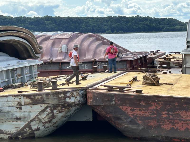 Two workers manage barges headed for St. Paul, Minnesota as the pilot boat pushes them up the Mississippi River after passing through the lock at Lock & Dam 13 near Fulton on Sunday, July 6, 2025.