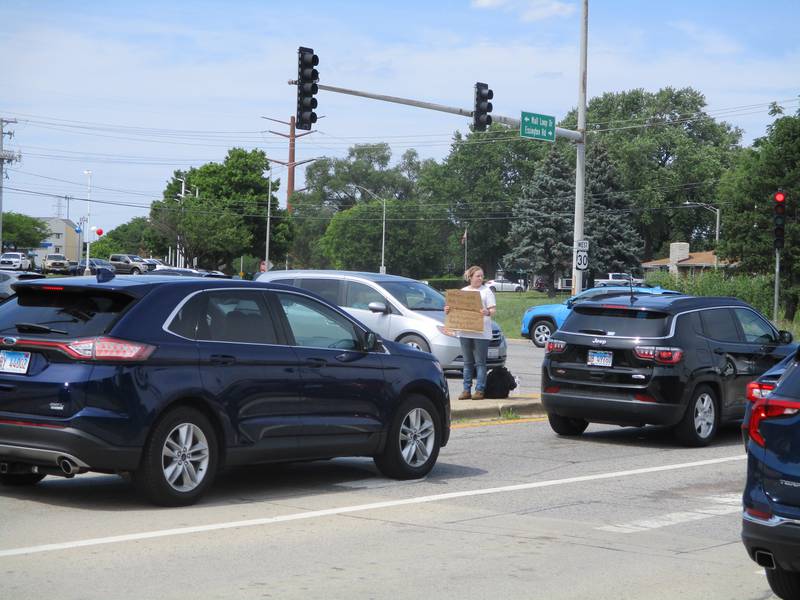 Ashley Hill stands on a raised median while holding a sign asking for money on Mall Loop Drive outside the Louis Joliet Mall in Joliet on July 2, 2022.