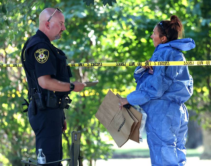 A DeKalb County sheriff’s deputy talks to an investigator in a protective suit Tuesday, Sept. 30, 2025, in front of a house in the 1300 block of Oakland Drive in Sycamore where two people were found dead Tuesday morning.