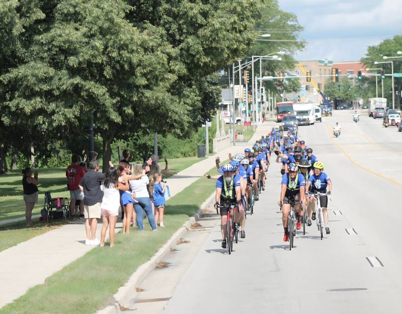 Onlookers wave to bicyclists as they make their way through downtown DeKalb along Lincoln Highway (Illinois Route 38) on Saturday, July 12, 2025. Nearly 100 cyclists biked from Normal to DeKalb on Saturday, July 12, 2025, for Cycle Across Illinois, a charity campaign to honor fallen police officers and raise funds for their families.