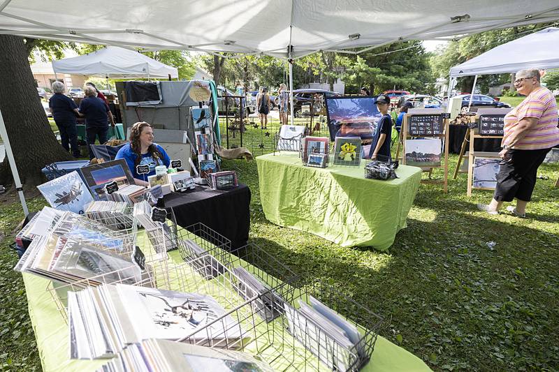 Nichole Kuzniewicz of Bettendorf works a booth with her photographs Saturday, July 6, 2024, during the Nuts About Art exhibit at John Dixon Park.