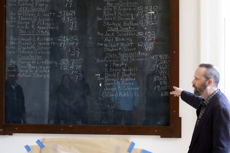 Woodstock City planner Darrell Moore talks about the newly remodeled Old Courthouse Center in Woodstock on Thursday, July 13, 2023, as people are reflected in the saved had written vote totals during a tour of the building.